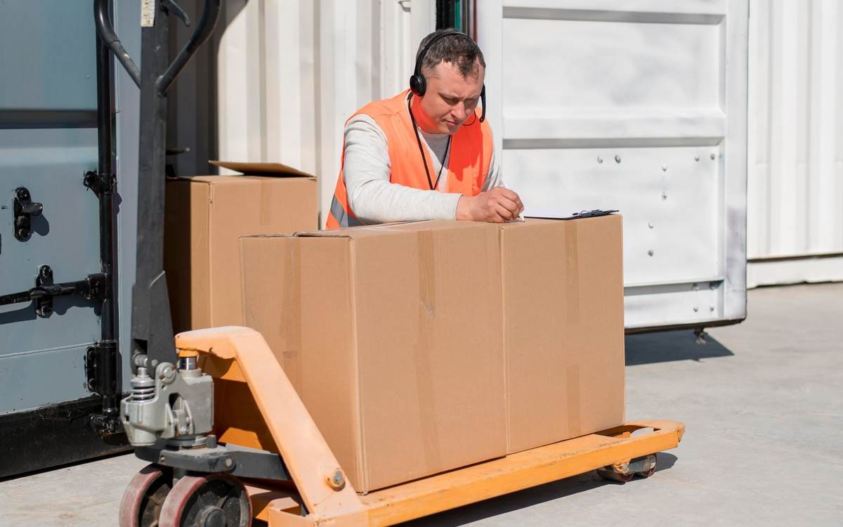 A worker checking boxes on a pallet jack